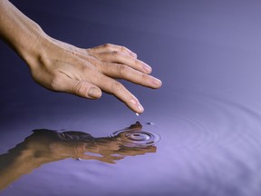 human hand touching the surface of a clear pond of water
