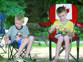 Kevin Birley  7, left, and his older brother Mikey 8,  pick a quiet spot in the shade and comfy chairs so they could whittle their sticks, collected on a family camping trip.   POSTMEDIA