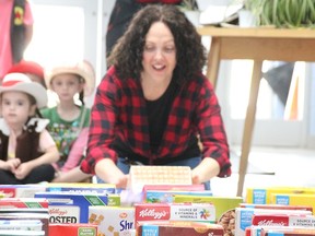 Erin Gower, principal at Sir John Moore elementary school in Corunna, pushes a box of cereal to make the 1,125 boxes the school collected for the Inn of the Good Shepherd's food bank fall like dominoes Friday, May 19, 2023. (Tyler Kula/ The Observe)