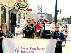 Michelle Lamont (left) holds the Women's House banner with Executive Director Marcy Stocking while Constable John Martin and Auxiliary Officer Matt Drost from the Saugeen Shores Police Service hold up placards at the Walk a Mile in Her Shoes event in downtown Port Elgin Saturday afternoon. Greg Cowan/The Sun Times