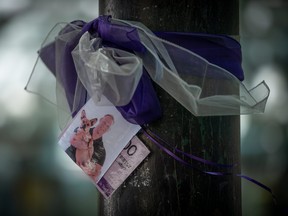 A photograph of a person who died due to an illicit drug overdose is tied to a tree with a purple ribbon by members of Moms Stop the Harm, in Vancouver, on Tuesday, August 16, 2022.