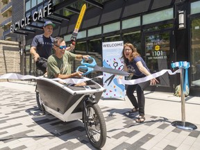London Bicycle Café co-owner Andrew Hunniford pilots a cargo bike while holding "the sword of traffic calming" as his business partner Andrew McClenaghan cuts the ribbon on their new location on Thames Street. Molly Miksa, executive director of London Cycle Link, cheers them on. Photo taken on Wednesday May 31, 2023. (Mike Hensen/The London Free Press)
