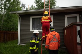 Firefighters from Didsbury, Alta. and Sundre, Alta. remove a sprinkler that firefighters installed on the roof of a Fort Chipewyan, Alta. home on Thursday, June 15, 2023. Sprinklers connected to fire hydrants were installed on the roofs of homes near the treeline in case a nearby wildfire approached the community. Vincent McDermott/Fort McMurray Today/Postmedia Network