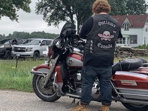 A man wearing an Outlaws motorcycle club vest watches OPP officers on the scene at a Melbourne home, southwest of London. Photo taken Tuesday, June 27, 2023. (Dale Carruthers/The London Free Press)