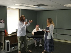 Two opera performers singing facing one another, while a pianist plays behind them.