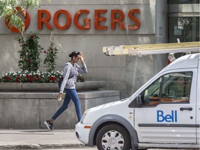 A pedestrian walks past the Rogers moniker with a Bell truck in the foreground, Monday July 11, 2022.