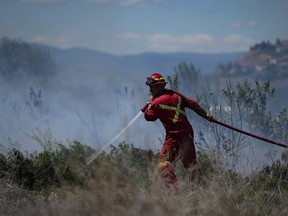 A firefighter directs water on a grass fire burning on an acreage behind a residential property in Kamloops, B.C., Monday, June 5, 2023. Climate experts say this summer of fires, floods and drought is far beyond the normal swings of Canadian weather