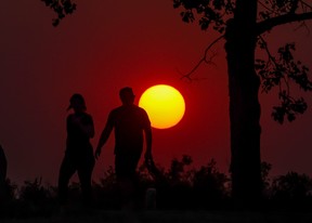 The forest fire smoke enhanced sun sets behind walkers on Tom Campbell’s Hill in Calgary on Wednesday, August 16, 2023. Gavin Young/Postmedia