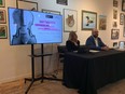 A man and a woman sitting at a table next to a TV in front of a wall of paintings.