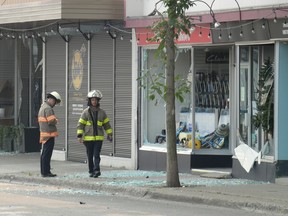 Two firefighters walk in front of a store with blown out windows