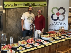 a man and woman stand behind a table filled with apples