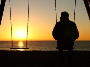 Stock phoot of man sitting on swing alone at sunset