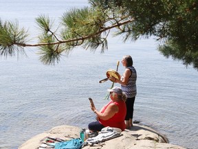 Linda Audette, standing, drums and sings while standing on a shoreline at Ramsey Lake in Sudbury, Ont., while Lori Millett-Porter looks on, on Tuesday August 8, 2023