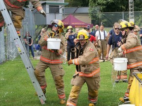 Courtland firefighter Kyle Godelie (left) lifts a bucket up to teammate Greg Vogrincic on the ladder, while Brandon Ronson (right) brings another bucket, and Andy Mater races to fill another during the Bucket Brigade relay Saturday in Vittoria. CHRIS ABBOTT