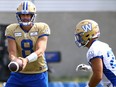 Quarterback Zach Collaros (left) holds the ball out for running back Brady Oliveira during Winnipeg Blue Bombers practice on Monday, Aug. 7, 2023.