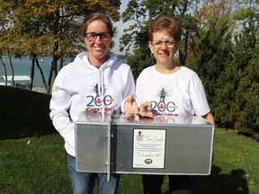 Corunna 200 committee member Melissa Atyeo, left, and chairperson Tracy Kingston hold a time capsule created as part of a year-long celebration of Corunna's heritage.  It's set to be opened in 50 years.