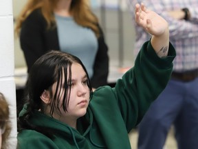 A girl in a green hoodie raises her hand to ask a question.