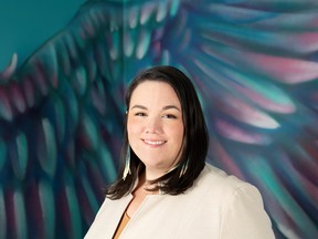 An Indigenous woman in a cream suit stands in front of a raven painting