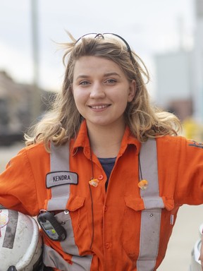 A woman in orange overalls smiles at the camera