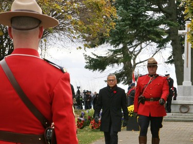 Kingston and the Islands member of Provincial Parliament Ted Hsu is accompanied by a member of the Royal Canadian Mounted Police after laying a wreath at the foot of the Cross of Sacrifice at Macdonald Memorial Park on Saturday as part of the city's civic Remembrance Day ceremony. A large gathering of military personnel, veterans, first responders, officials and residents attended the annual event on a cold but sunny morning. (Jan Murphy/The Kingston Whig-Standard/Postmedia Network)