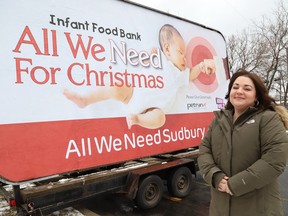 a woman stands in front of a billboard announcing the All We Need for Christmas fundraising campaign