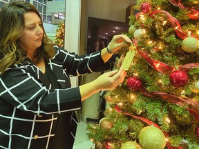 a woman places a gift tag on a Christmas tree