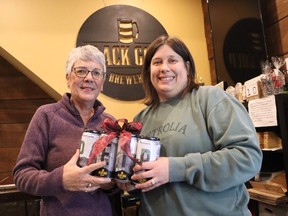Holding a special collection of cans at the Black Gold Brewery featuring labels with images from Petrolia's past are Denise Thibeault, left, head of the Petrolia 150th anniversary committee, and town marketer Laurissa Ellsworth.  Petrolis marks the 150th anniversary of its incorporation in 2024.