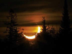 A partially-eclipsed sun rises over the trees in Marlbank, northeast of Belleville, Ont. Thursday, June 10, 2021. A solar eclipse occurs when the moon passes between Earth and the Sun.
