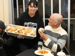 A woman serves a man a dinner roll at a soup kitchen