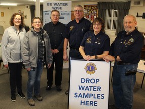 Organizers stand together in front of a sign directing participants to drop off their water samples.