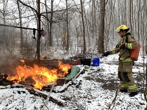 A Kingston firefighter extinguishes a tent fire at a homeless encampment in Belle Park in Kingston