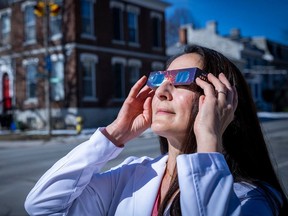 Dr. Yi Ning Strube, an associate professor in ophthamology at Queen's University, demonstrates the proper use of solar eclipse glasses in Kingston, Ont.
