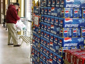 A shopper collects his purchases near packs of Pepsi and Coke soda at a market March 6, 2006 in Des Plaines, Ill. A New York Times report, produced in collaboration with the Fuller Project, traces sugar production in India's Maharashtra, where labour abuses are "endemic," to supply chains for the world's largest soft drink companies, PepsiCo and Coca-Cola. (Photo by Tim Boyle/Getty Images)