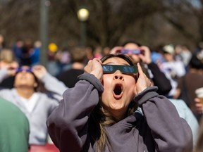 Hellen Liu looks at the solar eclipse through a friend’s viewing glasses at Western University in London on Monday, April 8, 2024. (Derek Ruttan/The London Free Press)