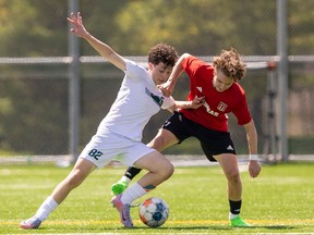 Gianluca DeCandido of the Mother Teresa Spartans, left, and Noah Bakke of the St. Thomas Aquinas Flames fight for the ball in a TVRA boys soccer game at Tricar Fields in London on Tuesday, April 30, 2024. The Spartans won 3-0. (Mike Hensen/London Free Press)