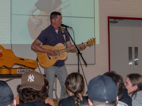 Nathan Crawford stands in front of a crowd of sitting students while playing the guitar.