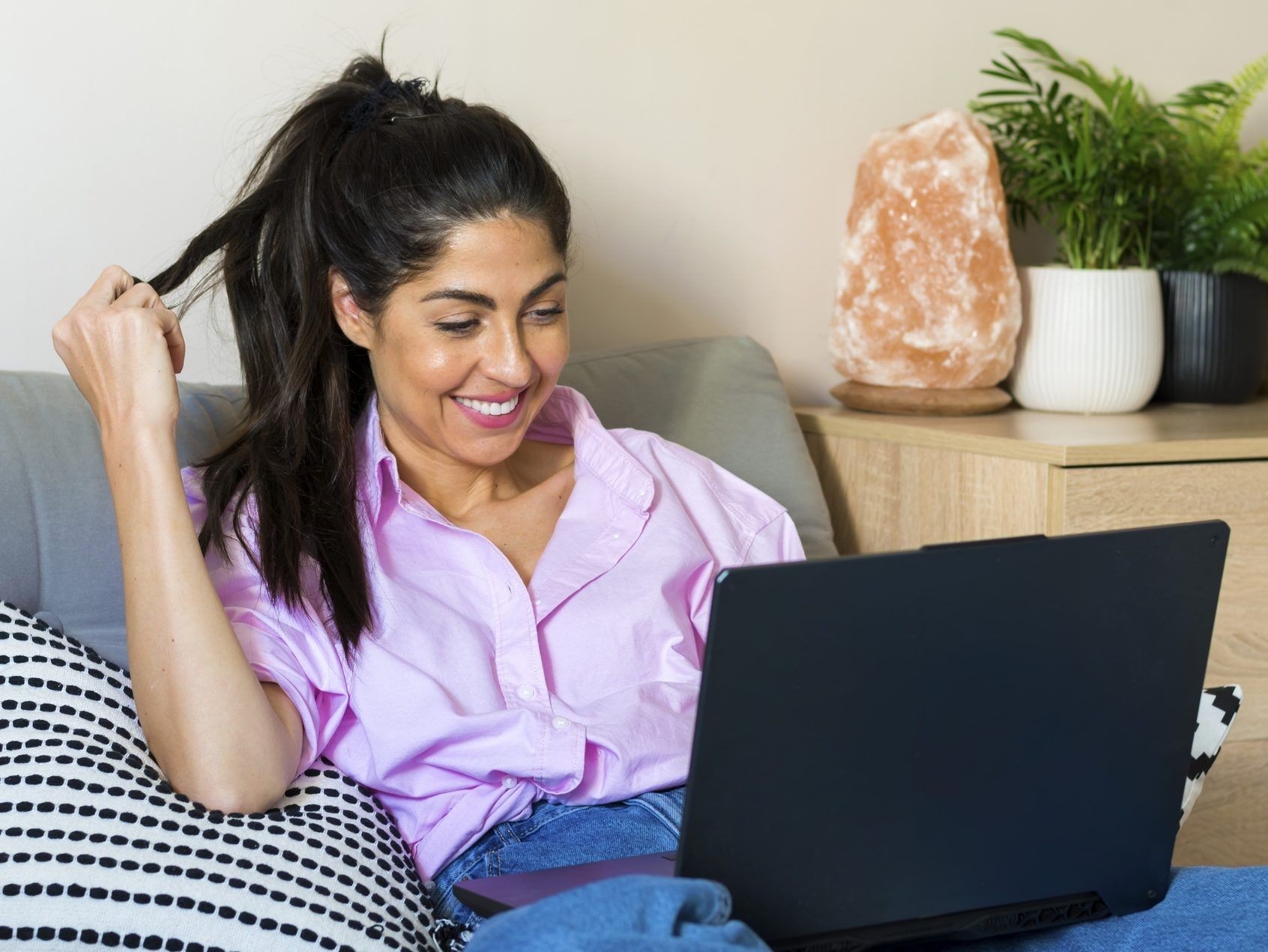 Beautiful, smiling young woman sitting at home while looking at laptop.