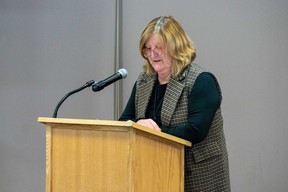 Higgs stands at a podium.