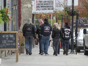 Four people with outlaw motorcycle gang patches on their jackets walk down a sidewalk