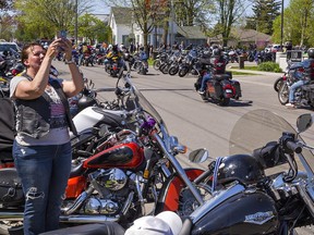 A woman stands next to a motorcycle holding up her phone to take a photo.