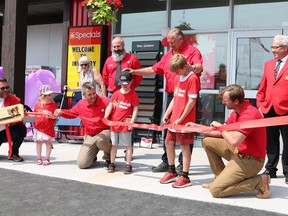 A red ribbon being cut by a little boy. People surrounding wearing red shirts