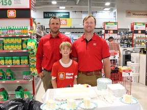 Three people in red standing in front of a cake.