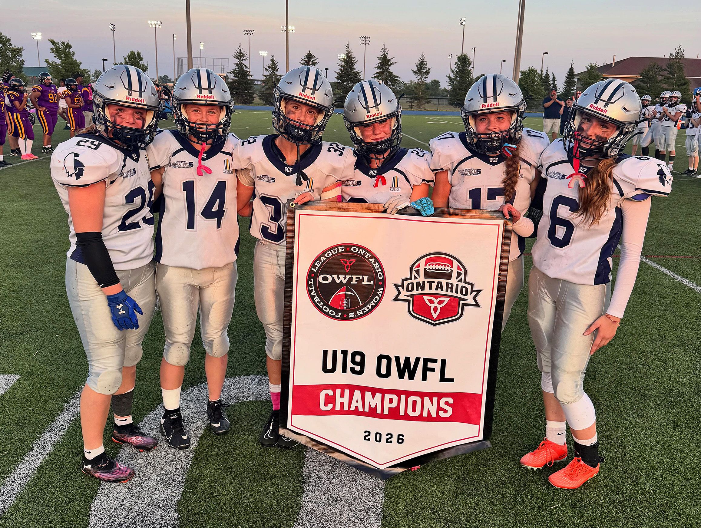 Players from the Sudbury Spartans 19U women's team celebrate with their Ontario Women's Football League Tier 1 championship banner