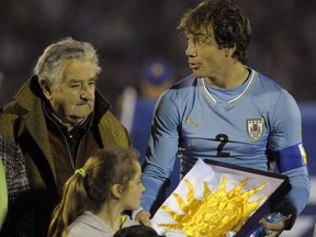FILE - In this June 4, 2014, file photo, Uruguay's President Jose Mujica, left, gives Uruguay's captain Diego Lugano the national flag before an international friendly soccer match against Slovenia in Montevideo, Uruguay. Uruguay's famously casual President is tossing some earthy expletives at FIFA as he welcomed Uruguay's team back from the World Cup oon Sunday June 29, over its four-month ban of Luis Suarez. Uruguayans overwhelmingly criticized FIFA's decision to ban Suarez from nine national team games and four months for biting an Italian defender. (AP Photo/Matilde Campodonico, File)