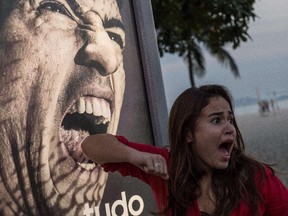 A tourist jokes in front of an advertisement with the portrait of Uruguay's forward Luis Suarez at Copacabana beach in Rio de Janeiro, Brazil, on June 26, 2014. Sportswear giant Adidas said Thursday it would stop using Luis Suarez, one of its key promotional stars, for World Cup adverts after his four-month ban from football activities for biting Italian Giorgio Chiellini. YASUYOSHI CHIBA/AFP/Getty Images
