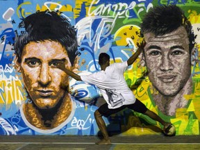 A youngster plays football in front of a mural of Argentine football player Lionel Messi (L) and Brazil's player Neymar da Silva Santos Junior at a field of Tavares Bastos shantytown (favela) in Rio de Janeiro, Brazil. (YOSHI CHIBA/AFP/Getty Images)