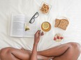 Person on bed with toast, tea, book, and glasses
