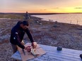 Elijah Qisiiq prepares a fish, lakeside.
