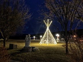 At night, The Children monument is illuminated beside a tipi.