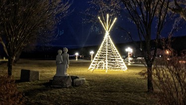 At night, The Children monument is illuminated beside a tipi.